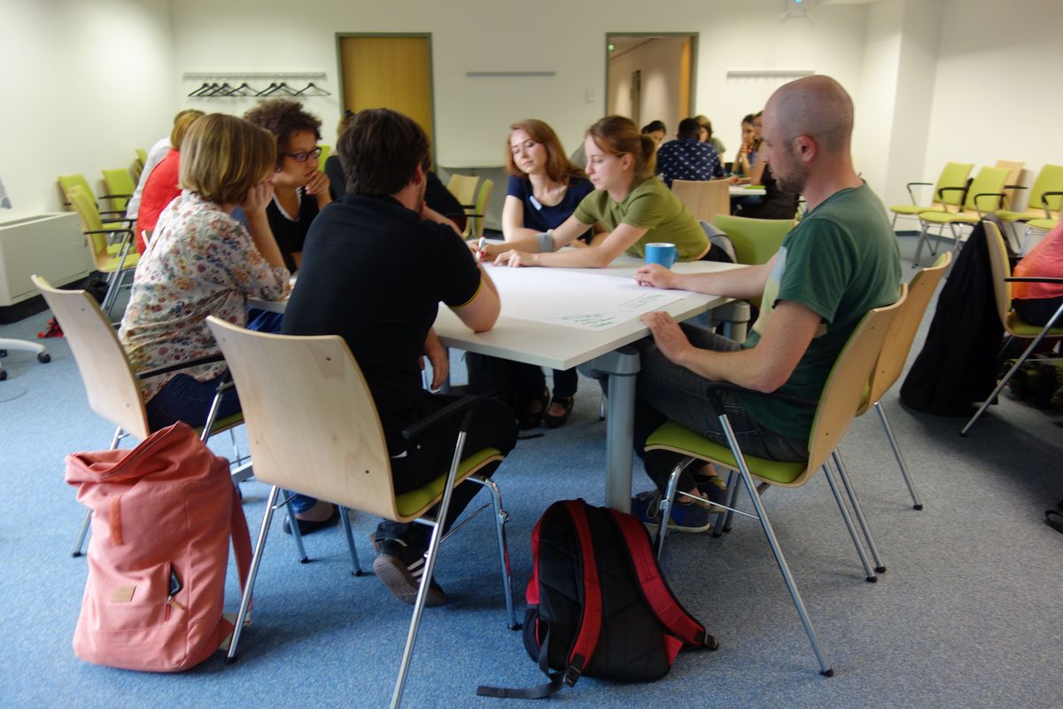 zur Vergrößerungsansicht des Bildes: Gruppe von Teilnehmenden sitzt bei der Summer School 2019 an einem Tisch und arbeitet