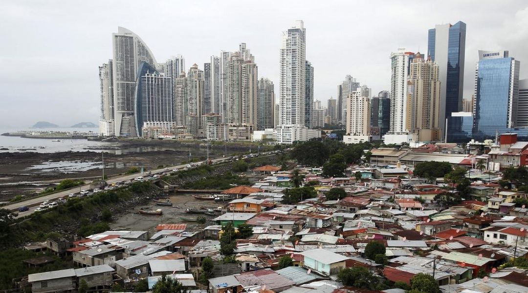 Blick auf dieSkyline von Panama City mit modernen Hochhäusern im Hintergrund. Im Vordergrund sind Hütten und ärmliche Behausungen abgebildet um den Kontrast zwischen Armut und Reichtum zu verdeutlichen.