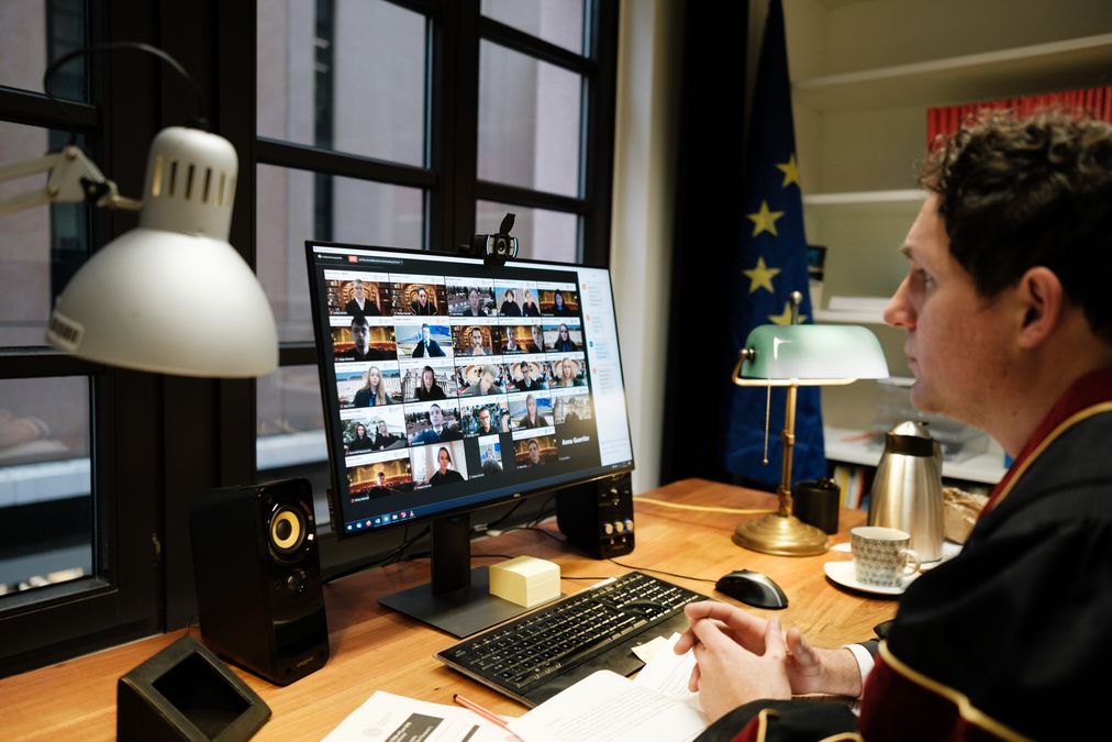 zur Vergrößerungsansicht des Bildes: Mann sitzt vor Computer, auf dem ein Zoom-Anruf mit Fotokacheln der Teilnehmenden geöffnet ist 